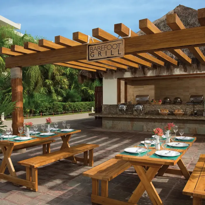Outdoor Barefoot Grill with picnic tables, wooden pergola, and tropical palm surroundings.
