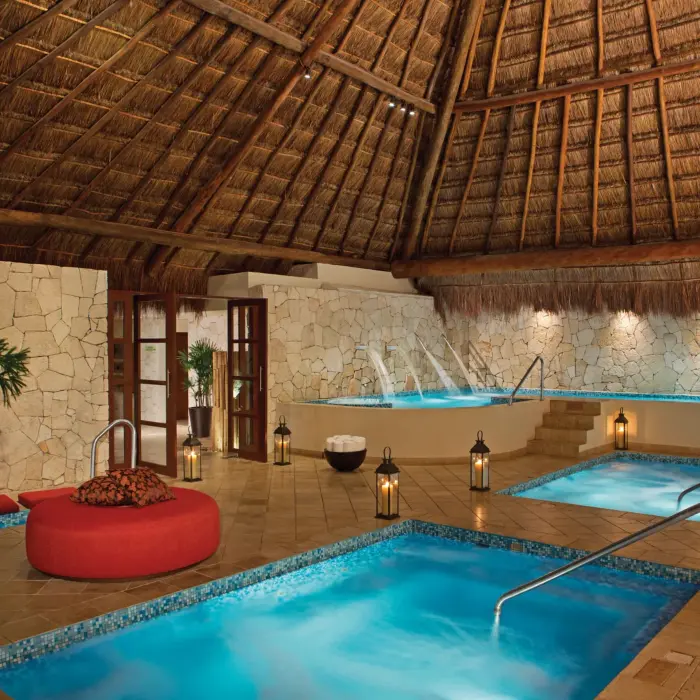 Indoor hydrotherapy spa circuit with warm plunge pools, stone walls, and thatched roof ambiance.