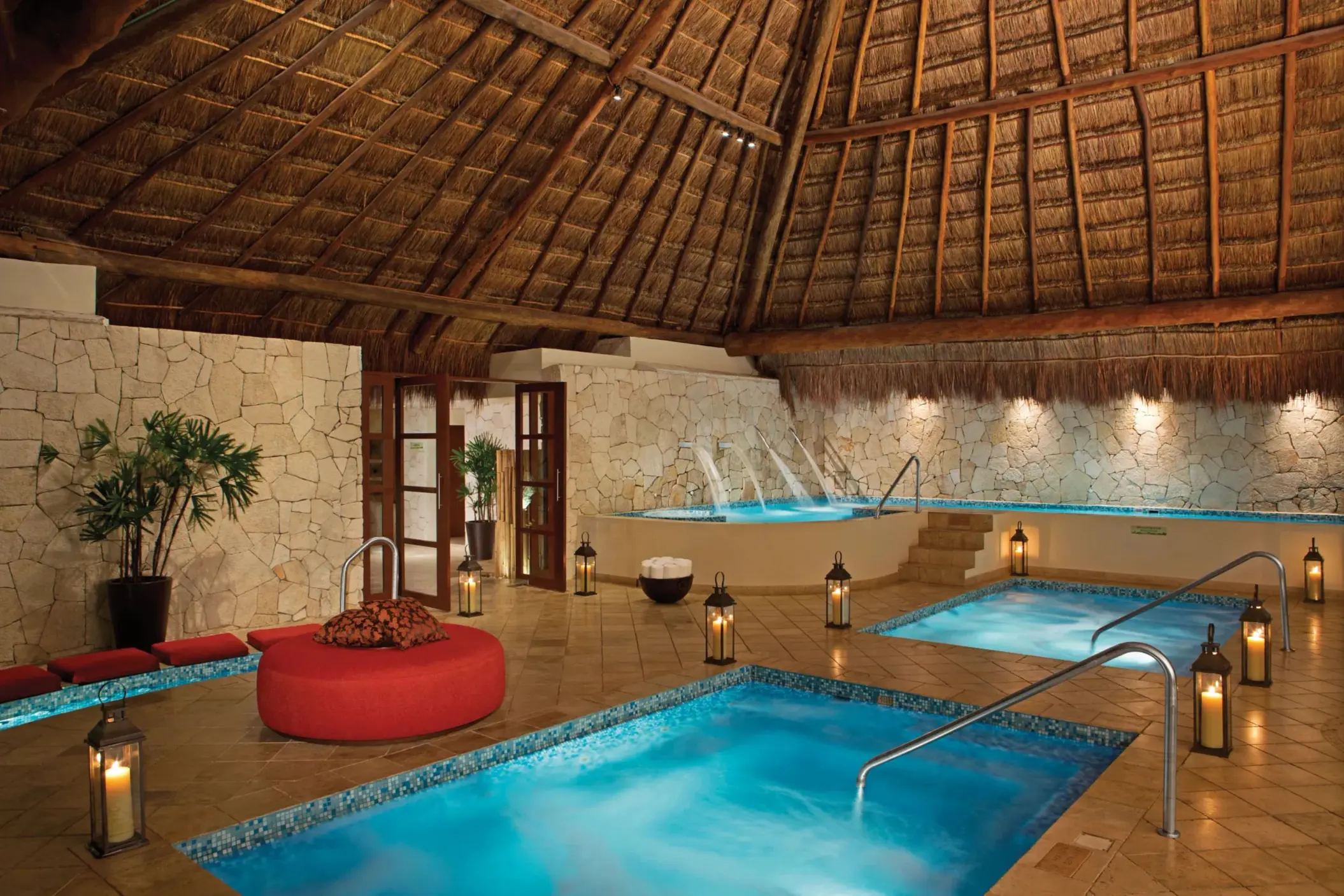 Indoor hydrotherapy spa circuit with warm plunge pools, stone walls, and thatched roof ambiance.