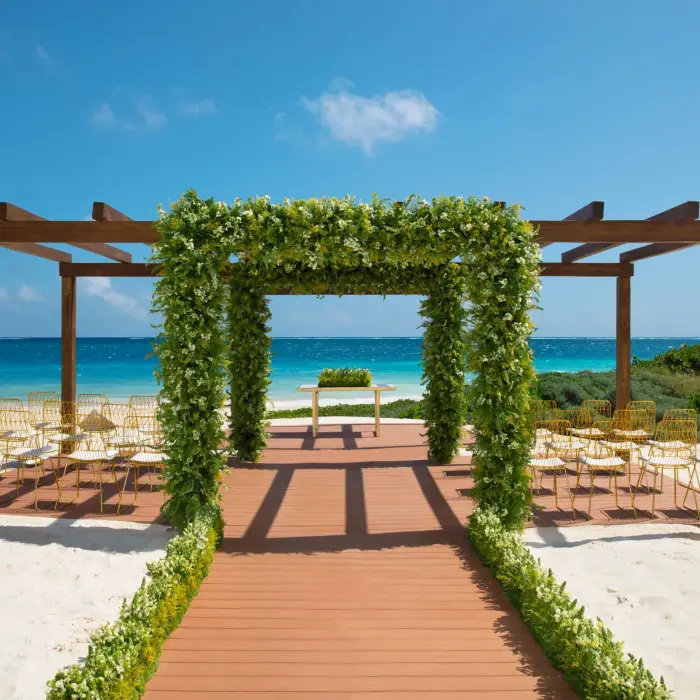 Beachfront wedding gazebo with floral arch, wooden aisle, and ocean backdrop.