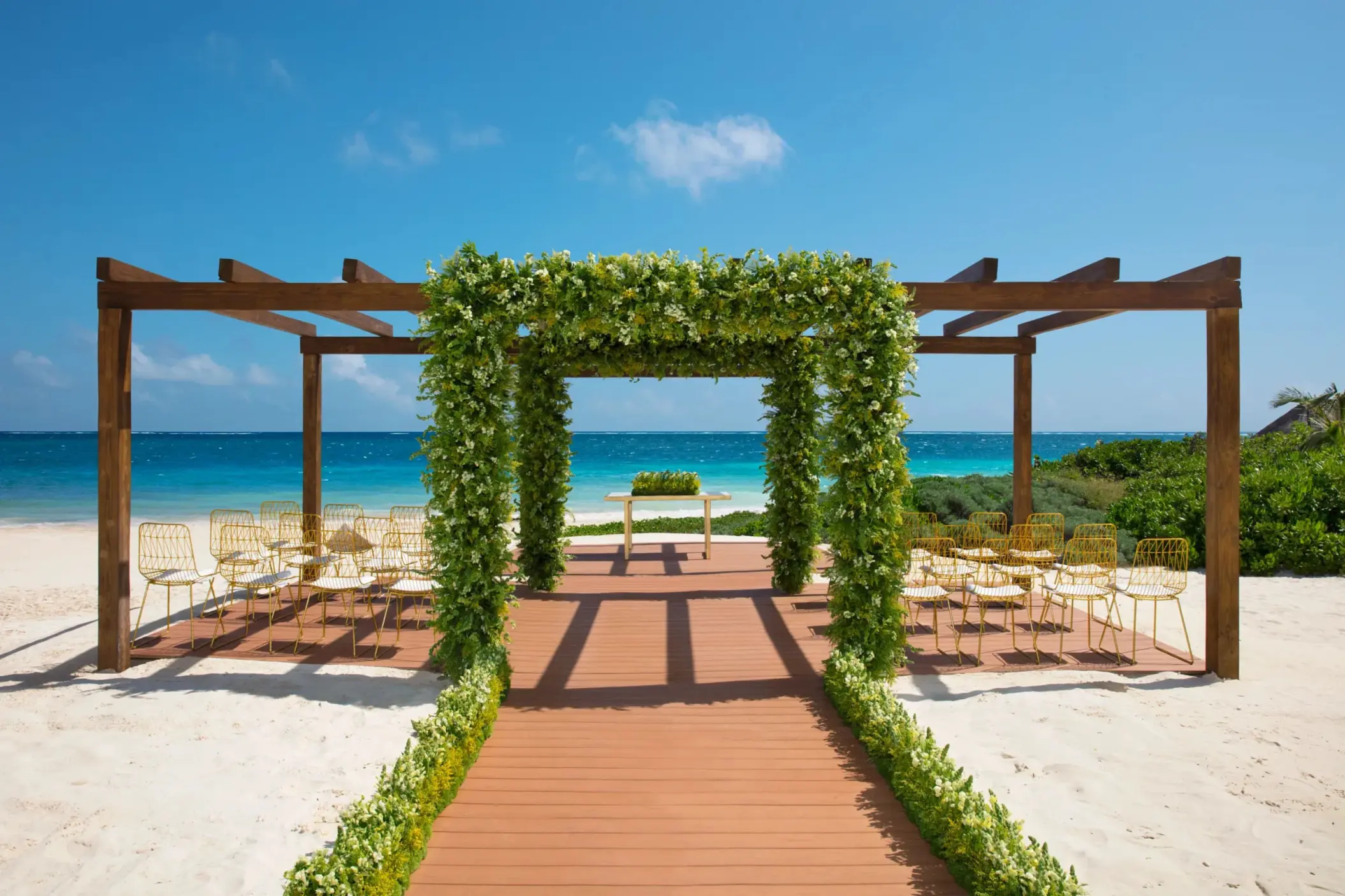 Beachfront wedding gazebo with floral arch, wooden aisle, and ocean backdrop.