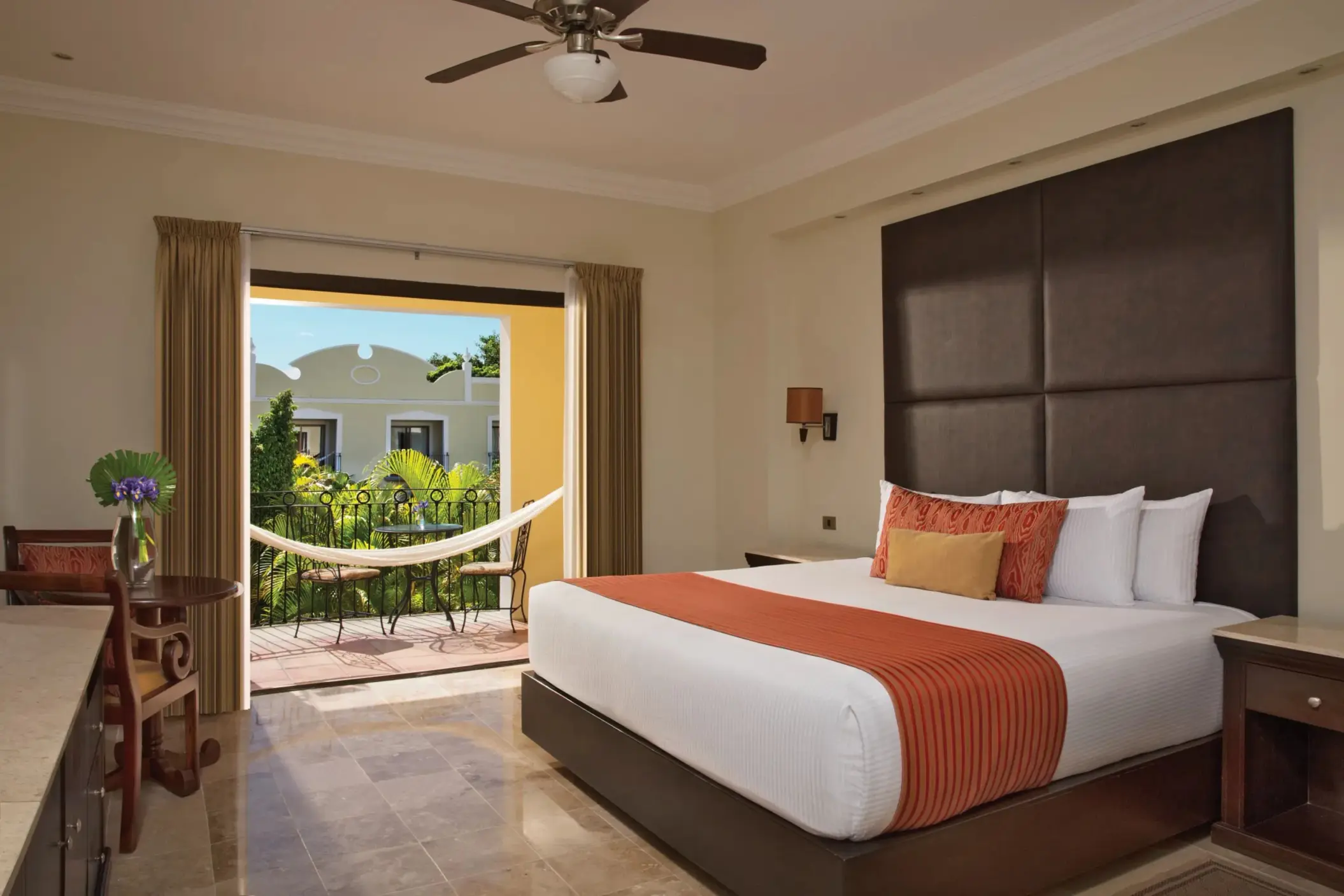 Elegant king bed room with orange accents, ceiling fan, and hammock on terrace.