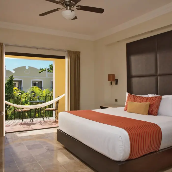 Elegant king bed room with orange accents, ceiling fan, and hammock on terrace.