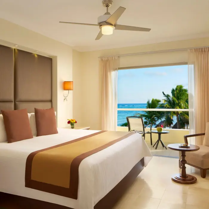 King bed ocean view room with neutral tones, tropical decor, and balcony seating.