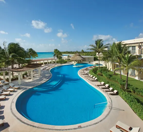 Large freeform pool at Dreams Tulum surrounded by sun loungers, palm trees, and beachfront rooms with ocean views.