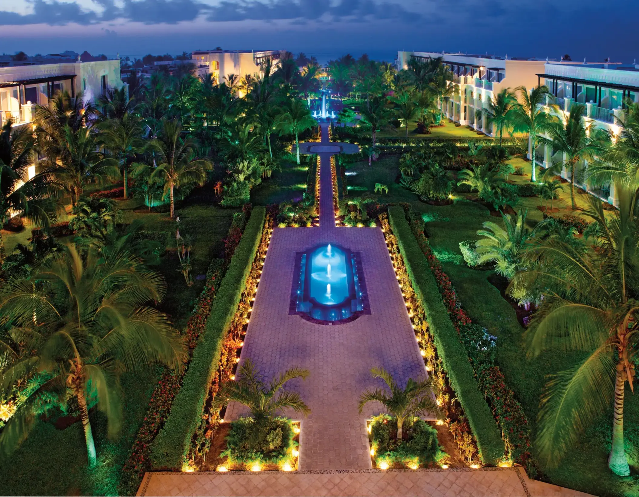 Dreams Tulum’s gardens illuminated at night with glowing fountains and palm trees creating a tropical ambiance.
