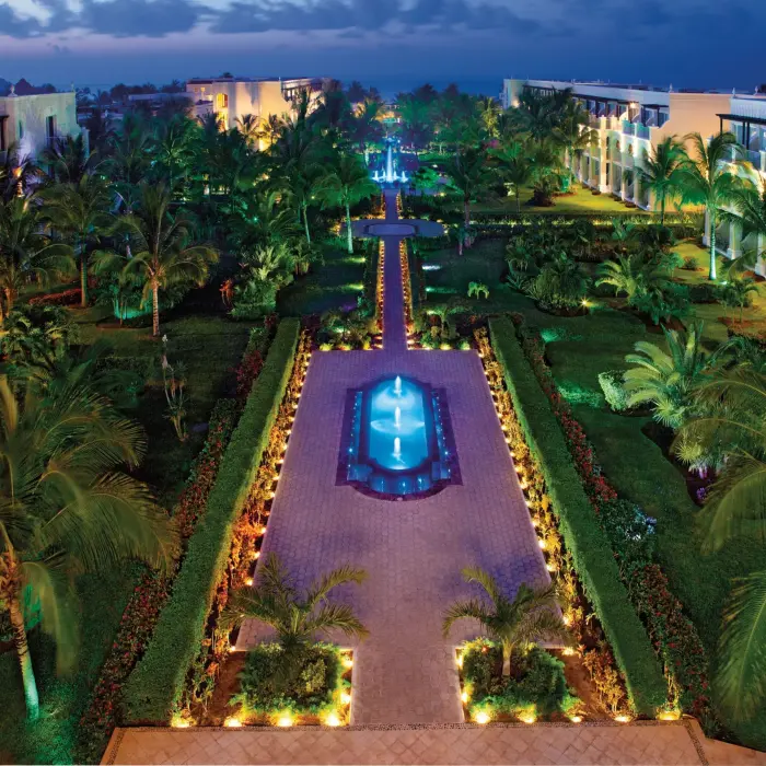 Dreams Tulum’s gardens illuminated at night with glowing fountains and palm trees creating a tropical ambiance.