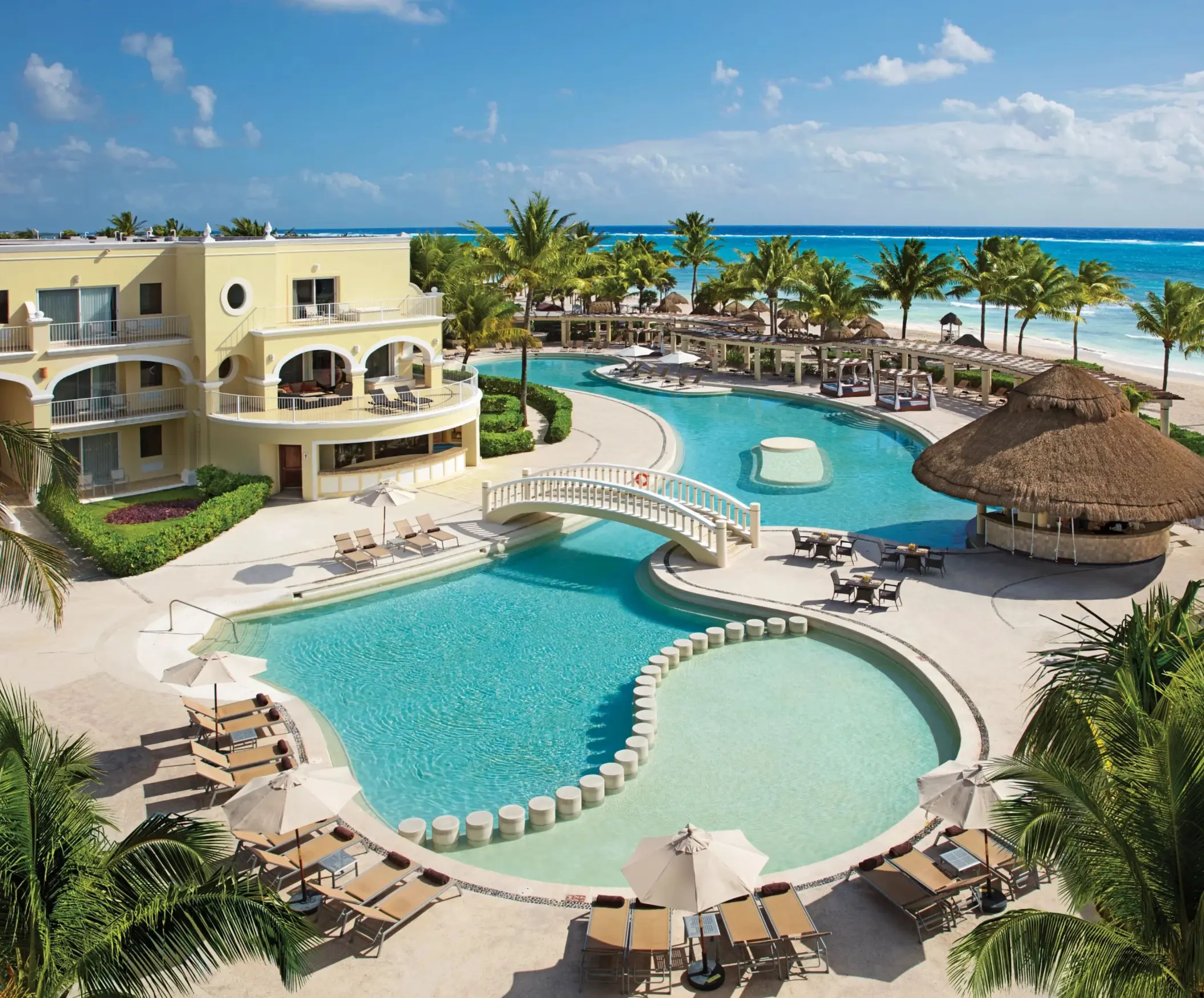Daytime panoramic view of Dreams Tulum’s main pool with bridge, palapas, and the turquoise sea in the background.