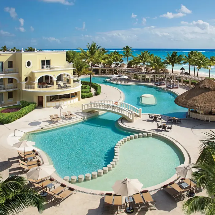 Daytime panoramic view of Dreams Tulum’s main pool with bridge, palapas, and the turquoise sea in the background.