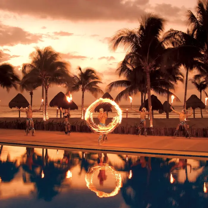 Fire dancers perform at sunset near the beach with palm trees silhouetted against a glowing sky.