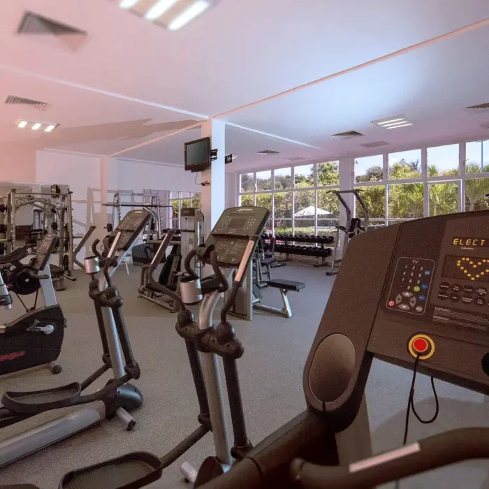 Modern fitness center with treadmills, ellipticals, weights, and large windows overlooking tropical greenery.