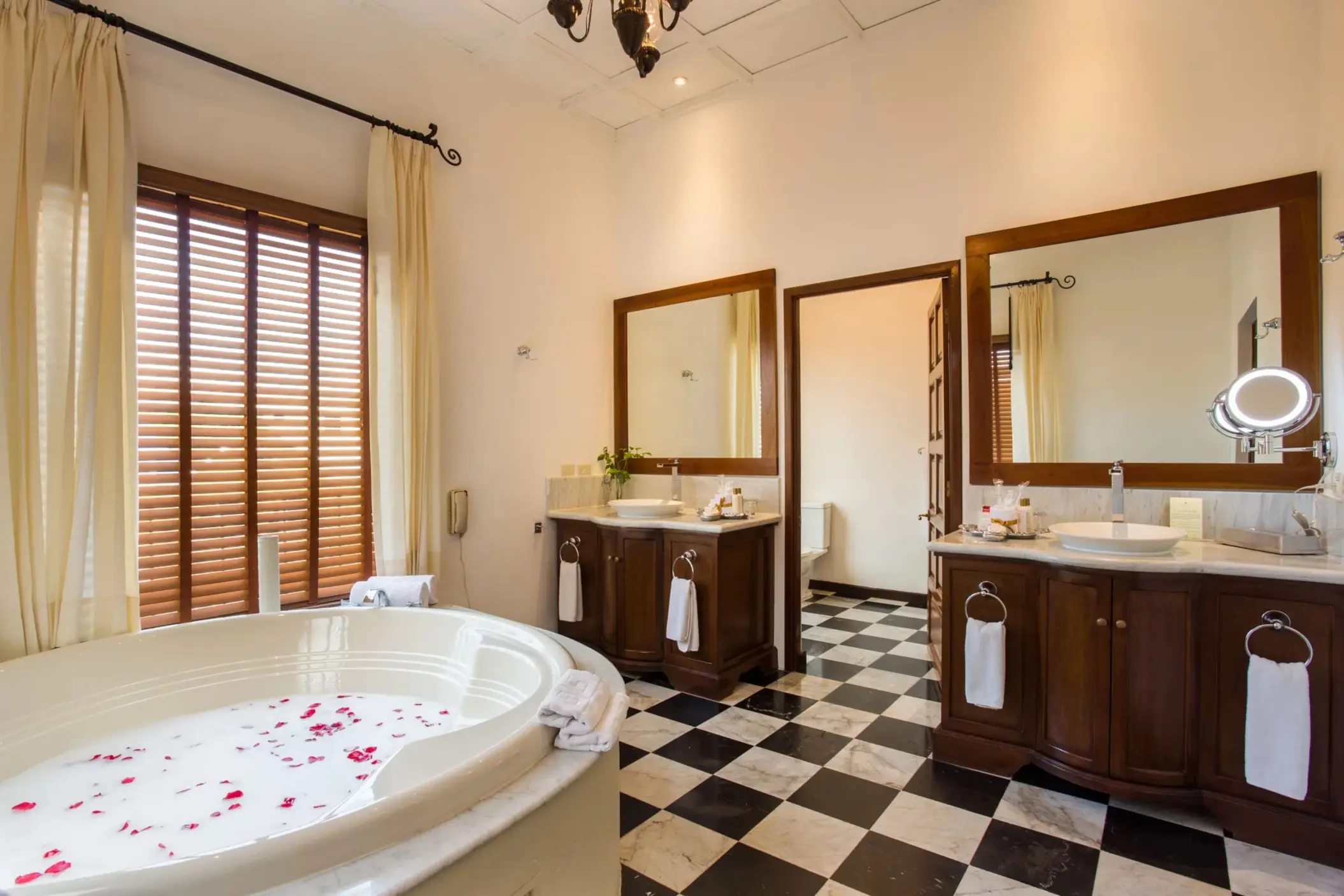 Classic bathroom with a large soaking tub filled with rose petals, double vanity, and checkered tile flooring.