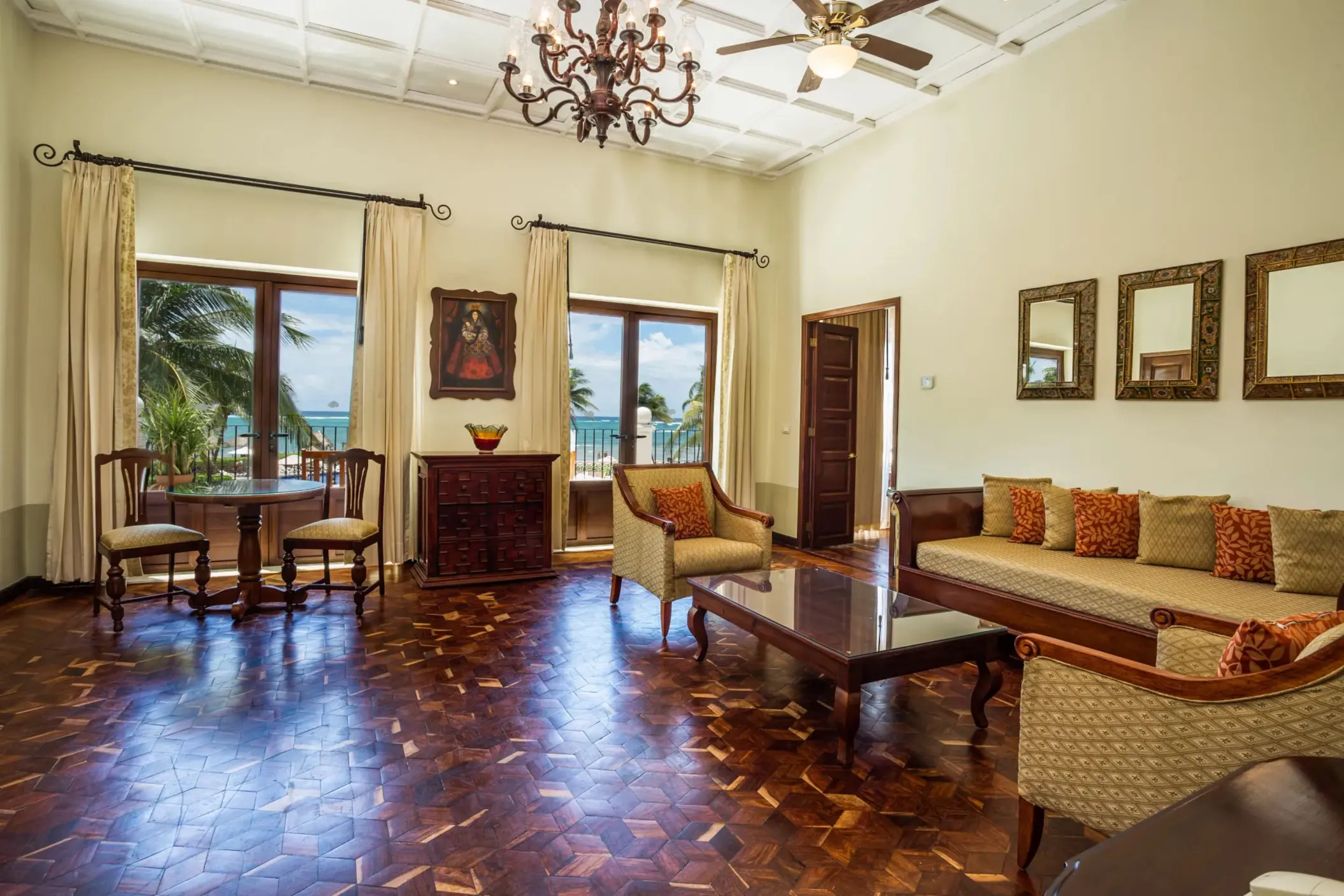 Colonial-inspired living room with ocean views, carved wood furniture, chandeliers, and balcony access.
