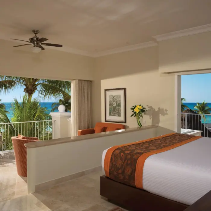 Spacious oceanfront room with king bed, seating area, and large balcony overlooking turquoise Caribbean waters.