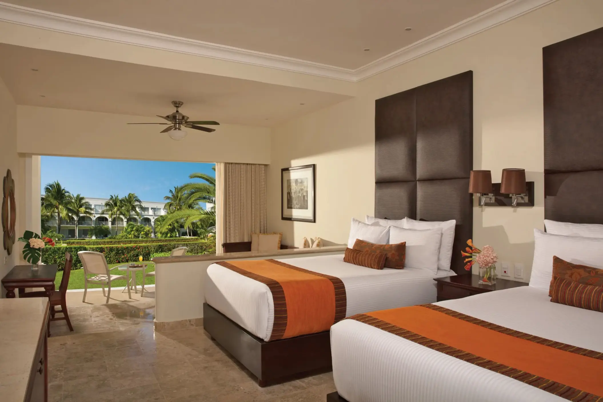 Garden-view room with two double beds, cozy seating area, and furnished terrace overlooking lush greenery.