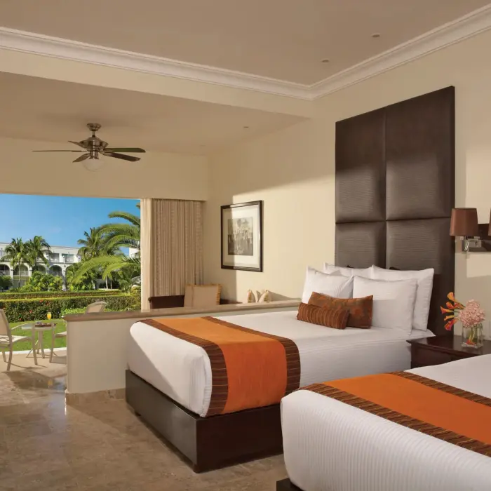Garden-view room with two double beds, cozy seating area, and furnished terrace overlooking lush greenery.