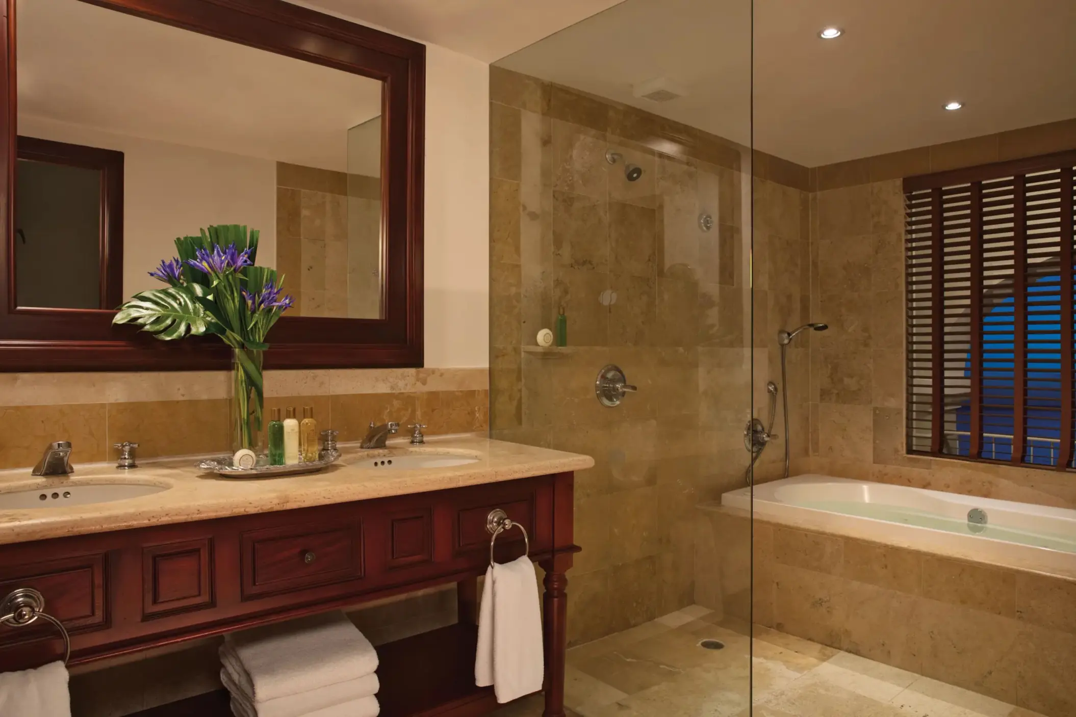 Spacious bathroom with granite double vanity, glass-enclosed shower, and soaking tub under wood shutters.