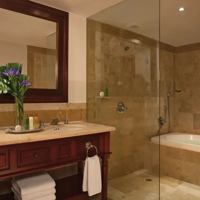 Spacious bathroom with granite double vanity, glass-enclosed shower, and soaking tub under wood shutters.