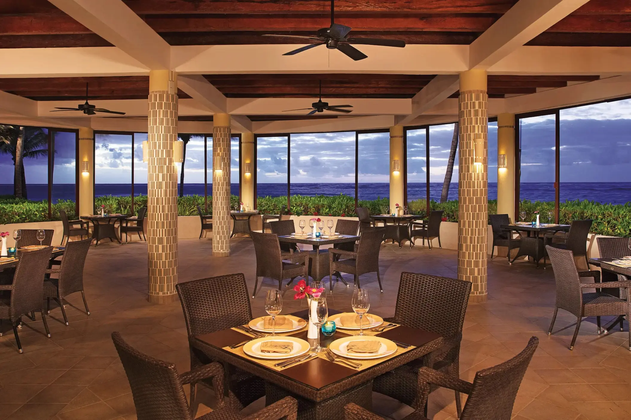 Seaside grill restaurant with ocean views, rattan chairs, and a romantic dinner setup.