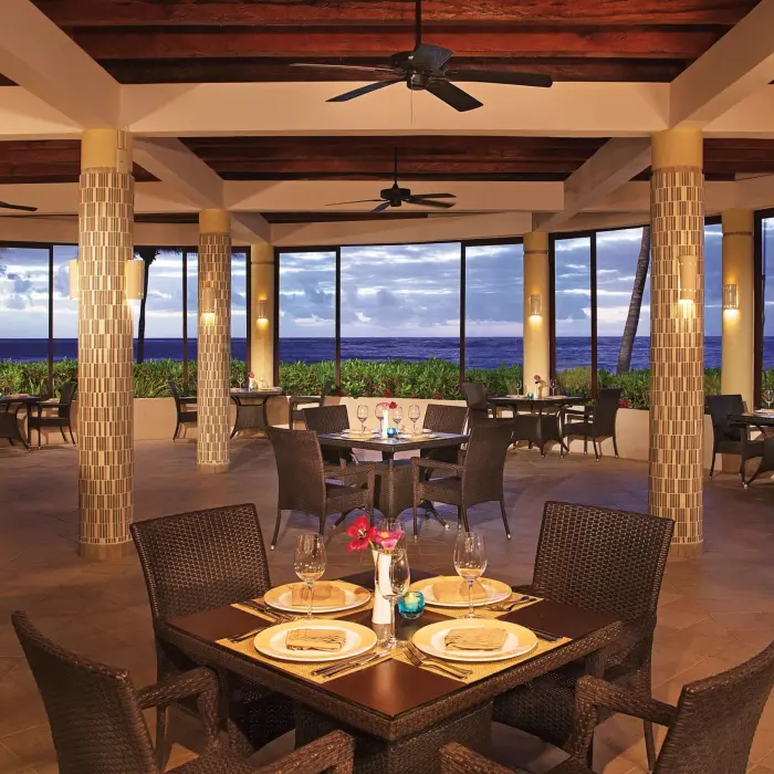 Seaside grill restaurant with ocean views, rattan chairs, and a romantic dinner setup.
