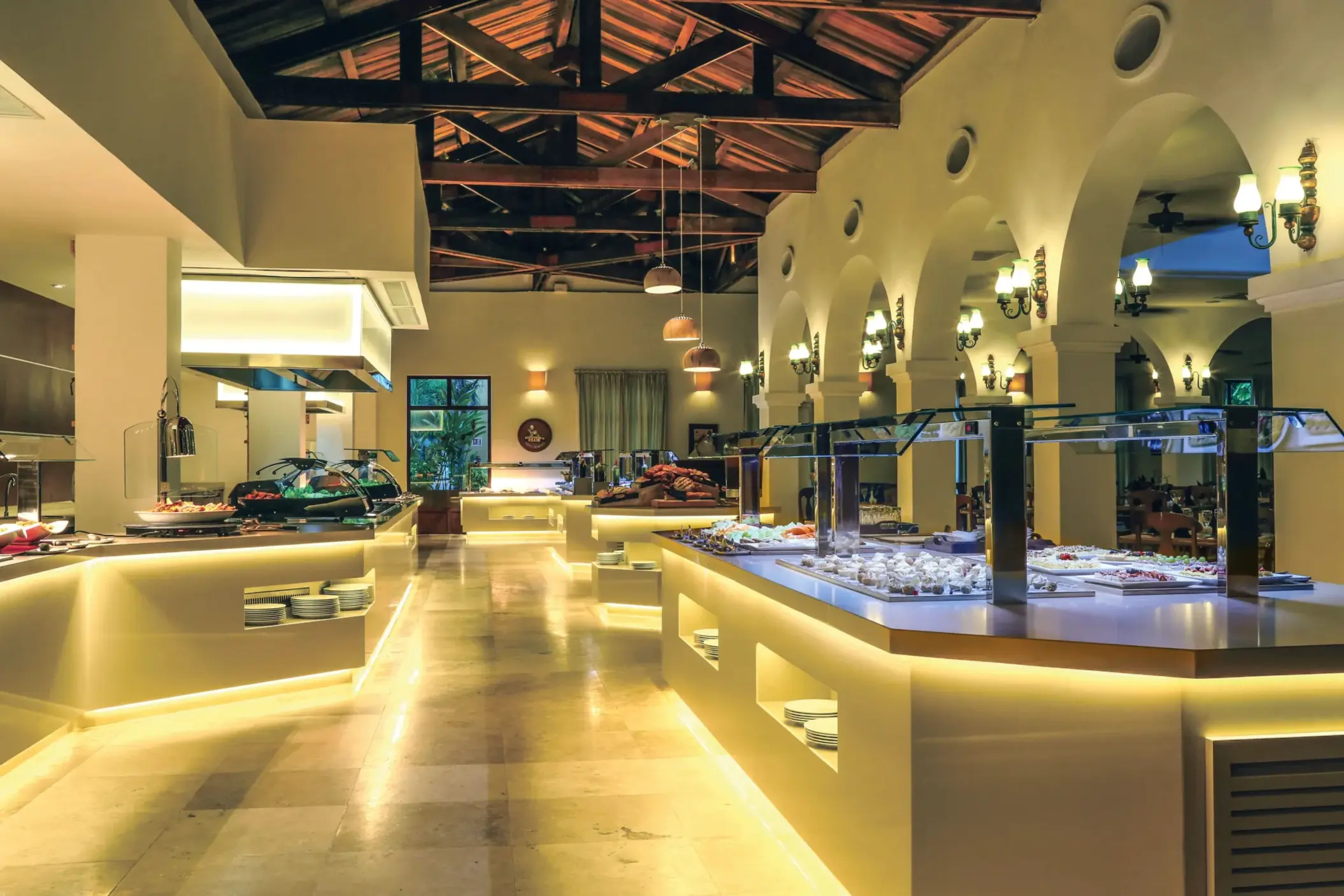 Modern buffet setup with glowing counters, high ceilings, and a wide variety of international cuisine stations.