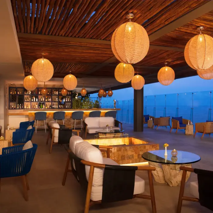 Elegant rooftop bar with cozy lounge seating, hanging lights, and sweeping views of the ocean.