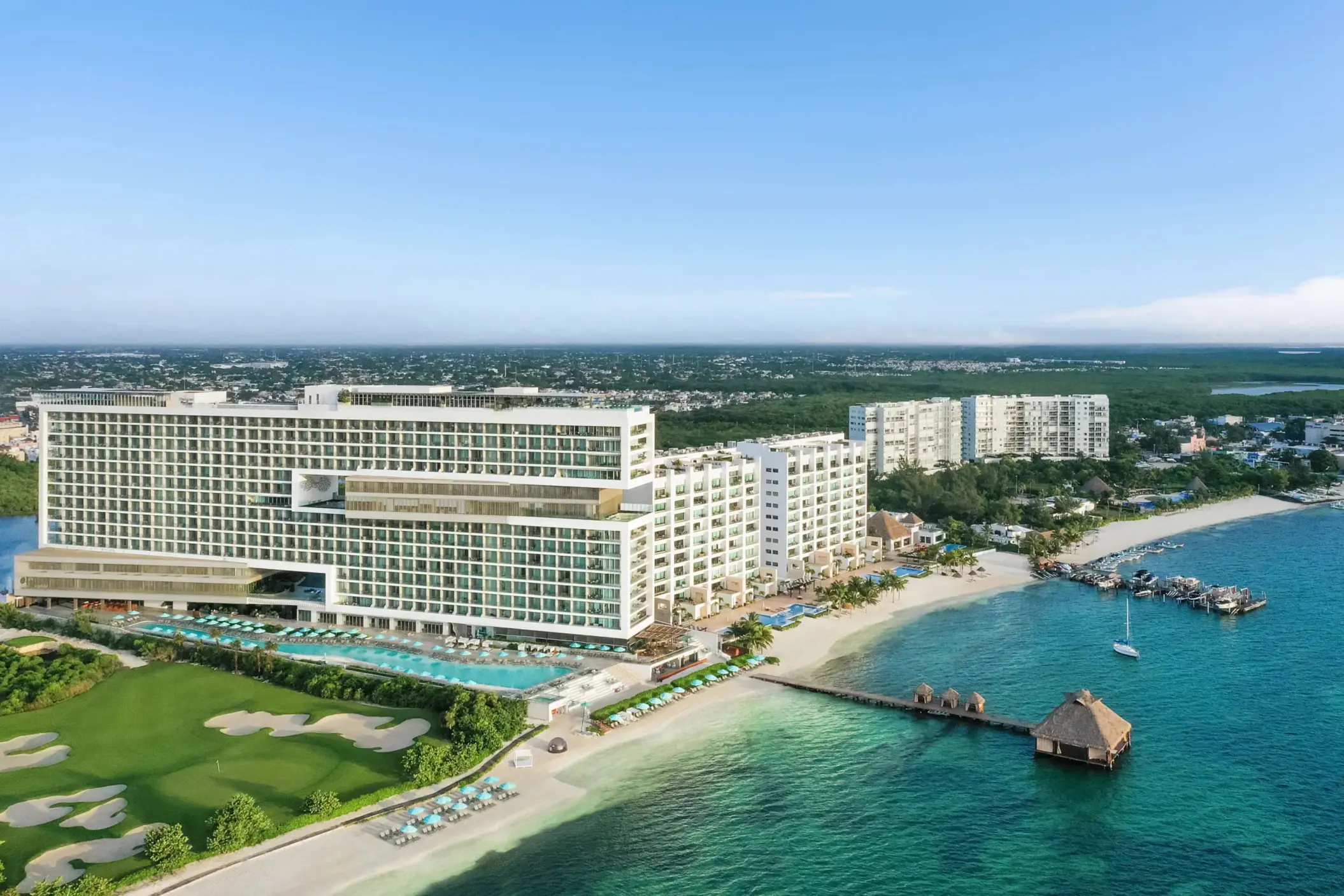Aerial view showcasing golf course, beachfront, and modern resort layout.
