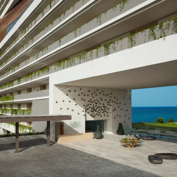 Modern resort entrance at Dreams Vista with ocean backdrop, hanging vines, and artistic wall decor.