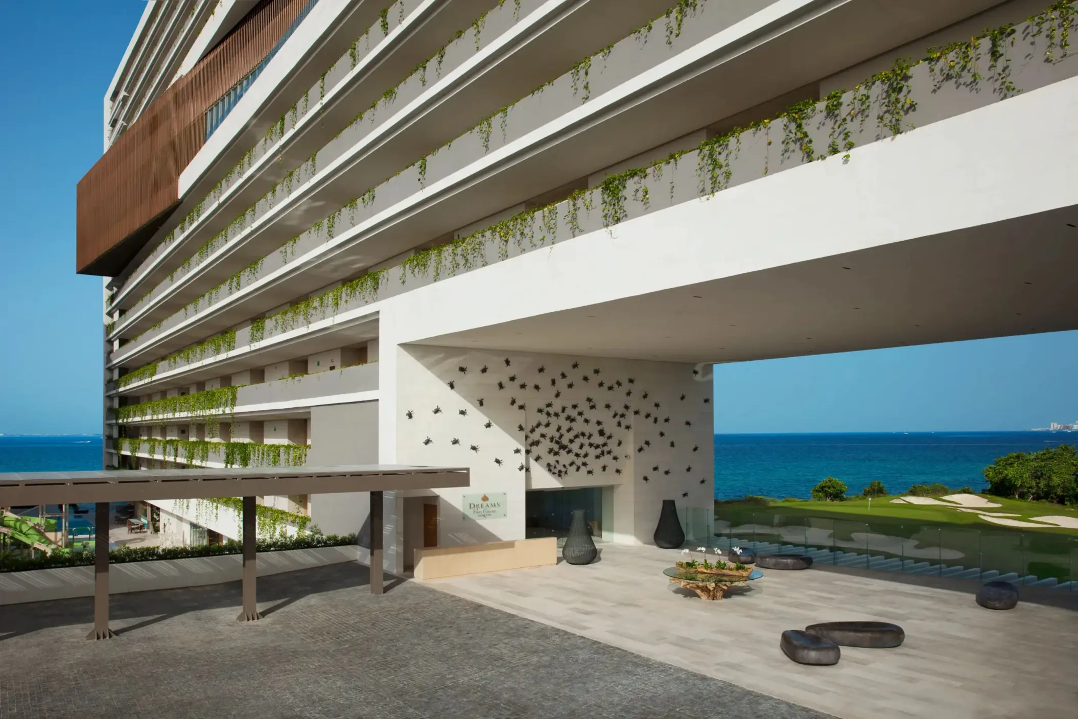 Modern resort entrance at Dreams Vista with ocean backdrop, hanging vines, and artistic wall decor.