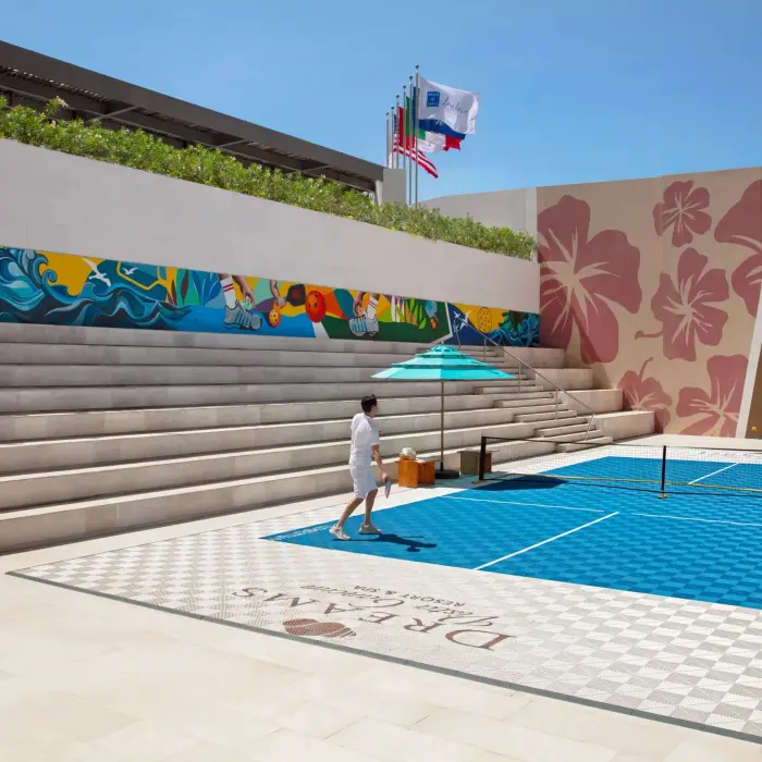 Outdoor pickleball court surrounded by stadium seating and colorful mural wall at Dreams Vista.