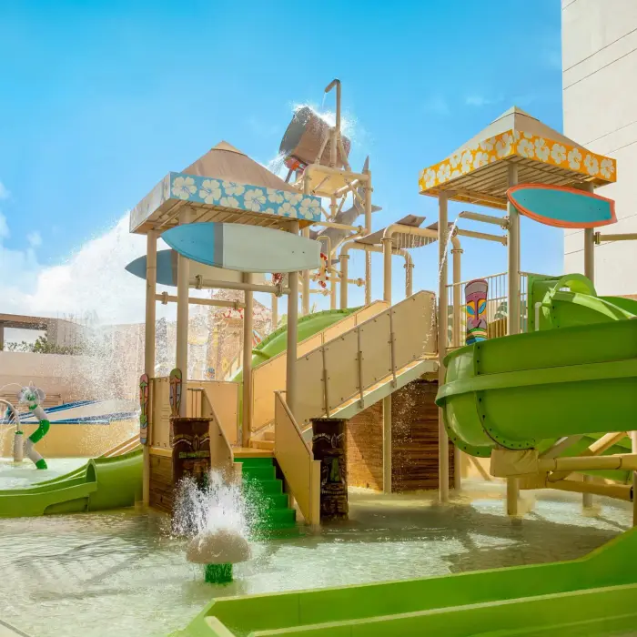 Surf simulator with instructor helping young guest ride the waves under vibrant mural walls.