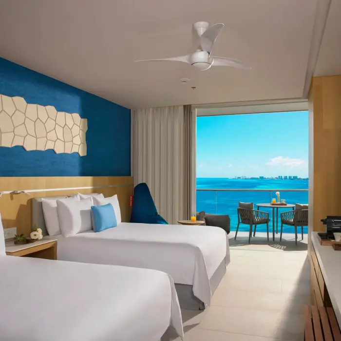 Family suite with two double beds, blue accent wall, and ocean view balcony at Dreams Vista Cancun.