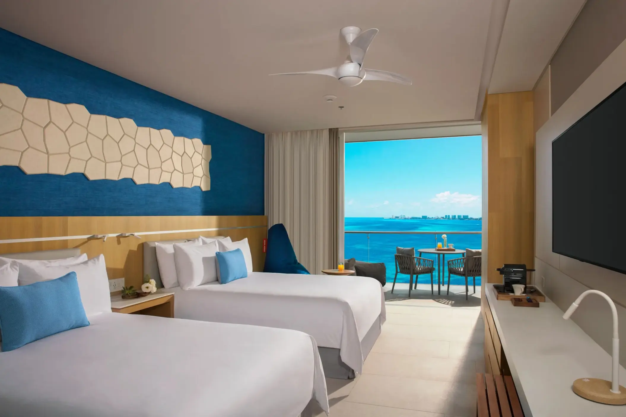 Family suite with two double beds, blue accent wall, and ocean view balcony at Dreams Vista Cancun.