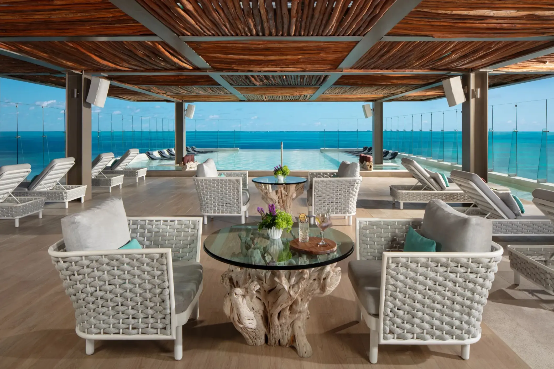 Rooftop pool lounge with lounge chairs and glass railing offering sweeping views of the Caribbean Sea.