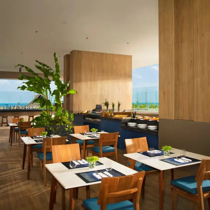 Open-air La Plaza dining area with buffet setup, natural wood decor, and green plants.