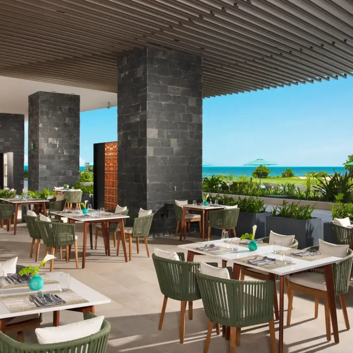 Outdoor La Terraza dining space with sleek tables, greenery, and ocean views.