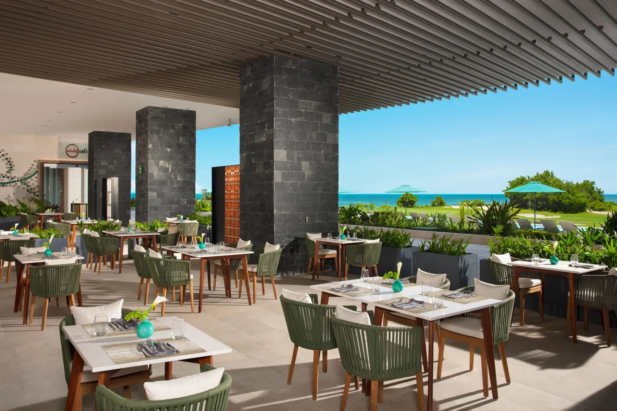 Outdoor La Terraza dining space with sleek tables, greenery, and ocean views.
