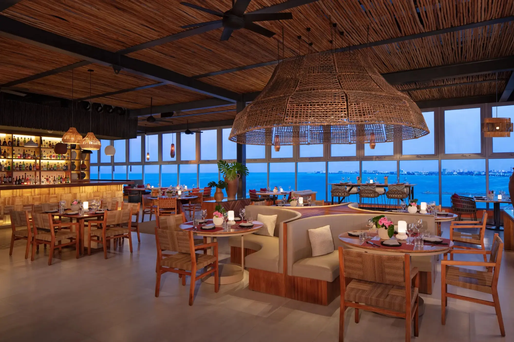Chic restaurant interior with round booths, woven ceiling and views of Cancun skyline.