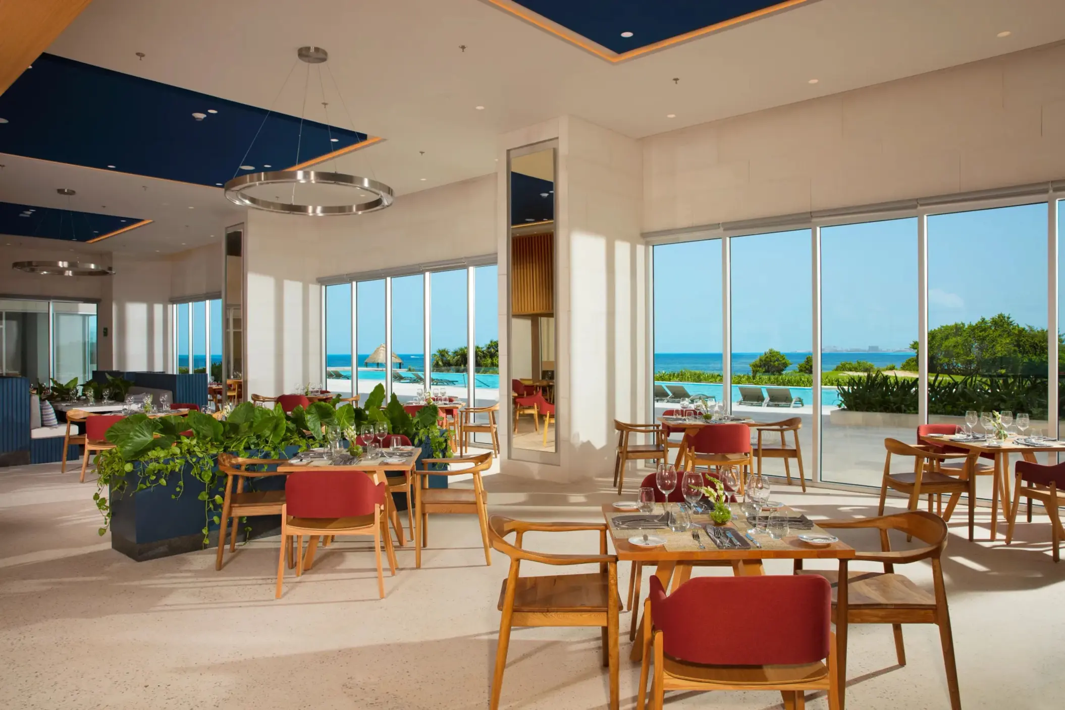 Bright restaurant interior with red chairs and ocean views through floor-to-ceiling windows.