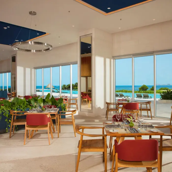 Bright restaurant interior with red chairs and ocean views through floor-to-ceiling windows.