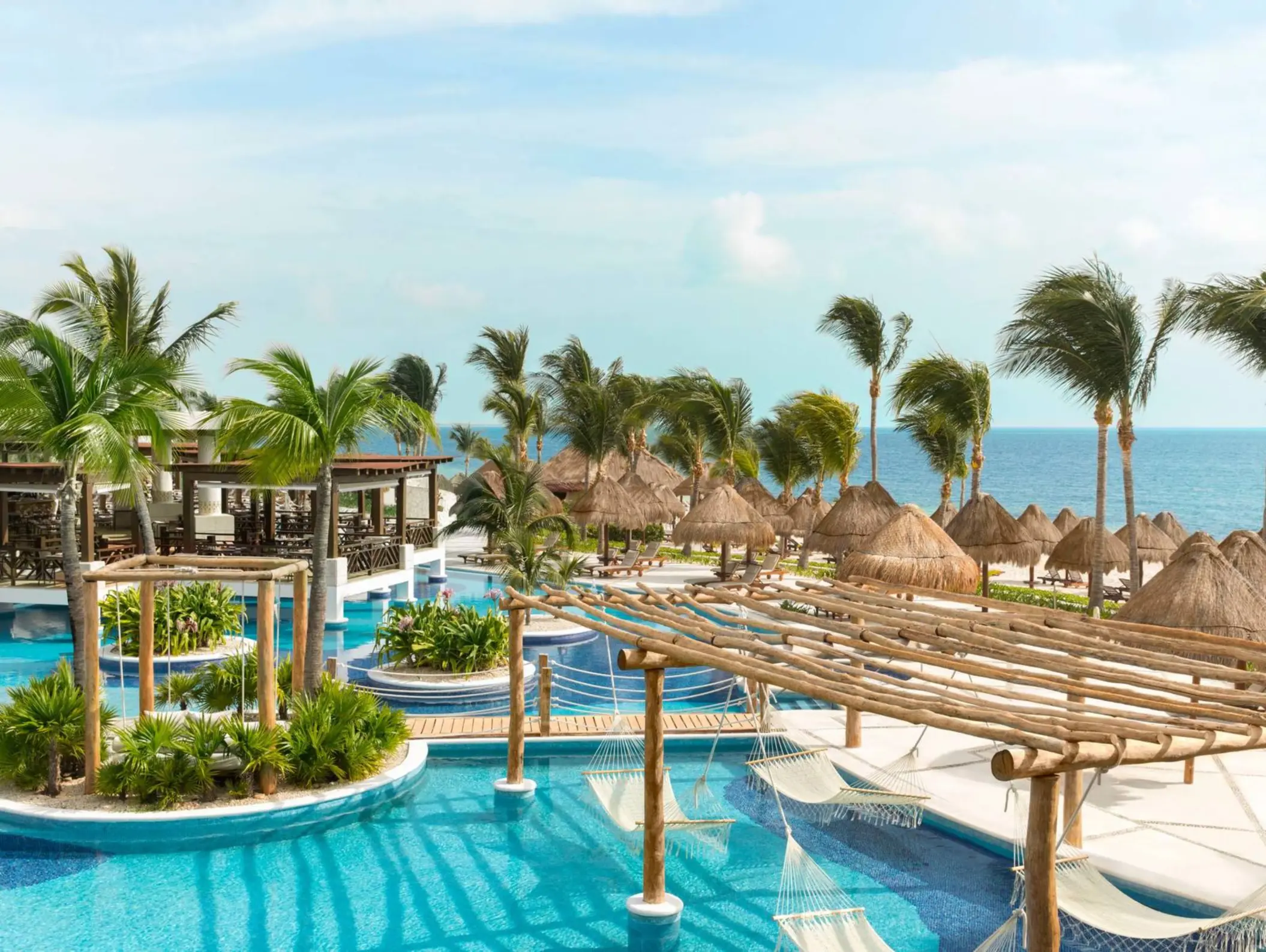 Overhead view of tropical pool area with hammocks, cabanas, and ocean backdrop at a Cancun resort.