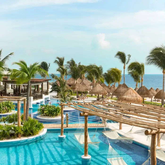 Overhead view of tropical pool area with hammocks, cabanas, and ocean backdrop at a Cancun resort.