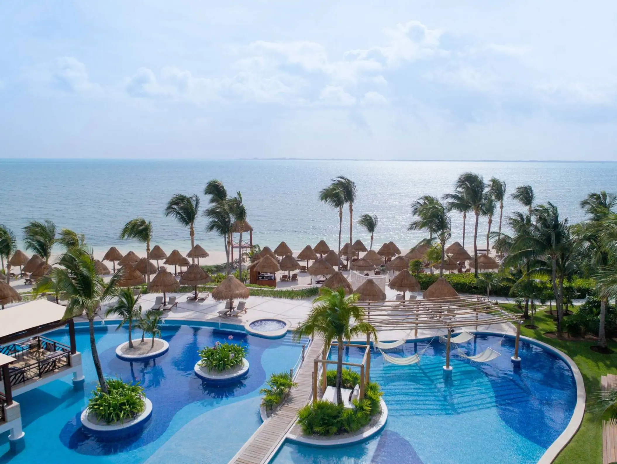 Vibrant poolside scene with lush greenery and wooden pergolas at Excellence Playa Mujeres resort in Cancun.