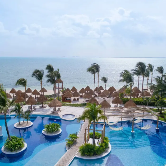 Vibrant poolside scene with lush greenery and wooden pergolas at Excellence Playa Mujeres resort in Cancun.