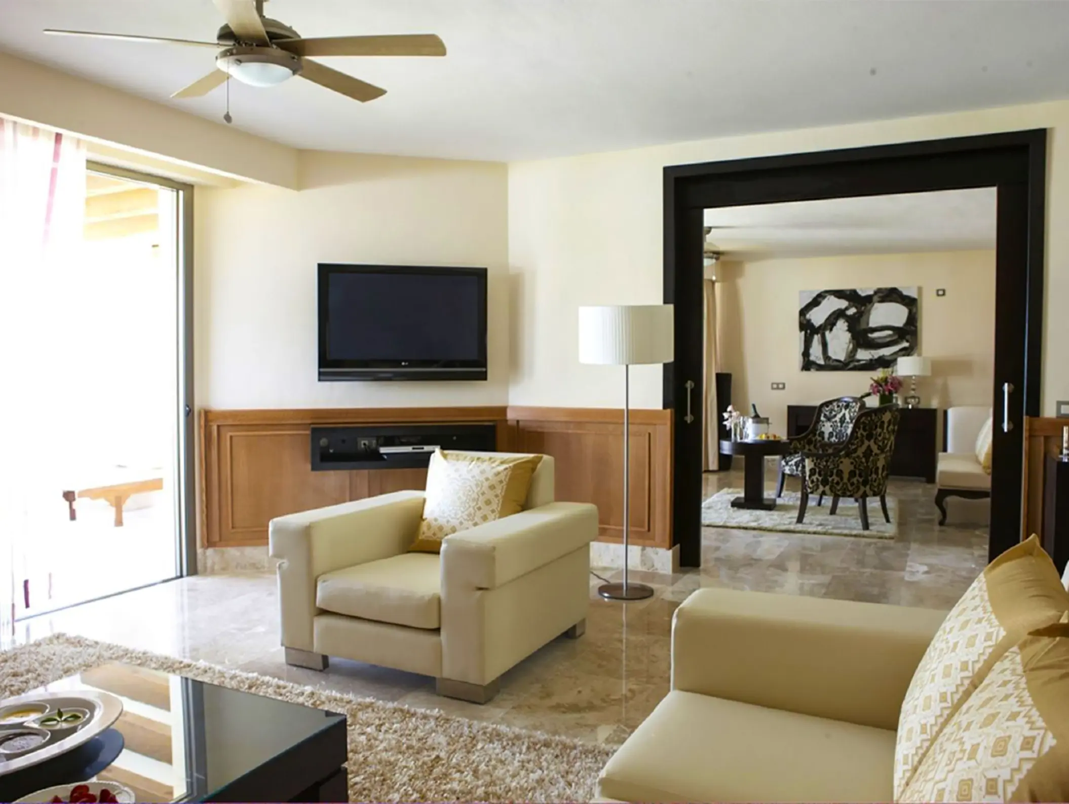 Spacious honeymoon suite living area with modern seating, marble floors, and flat-screen TV in Cancun.