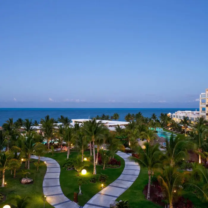 Twilight view over manicured resort gardens, ocean horizon, and suite balconies in Cancun.