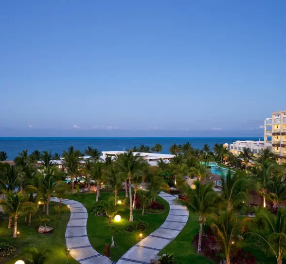 Twilight view over manicured resort gardens, ocean horizon, and suite balconies in Cancun.