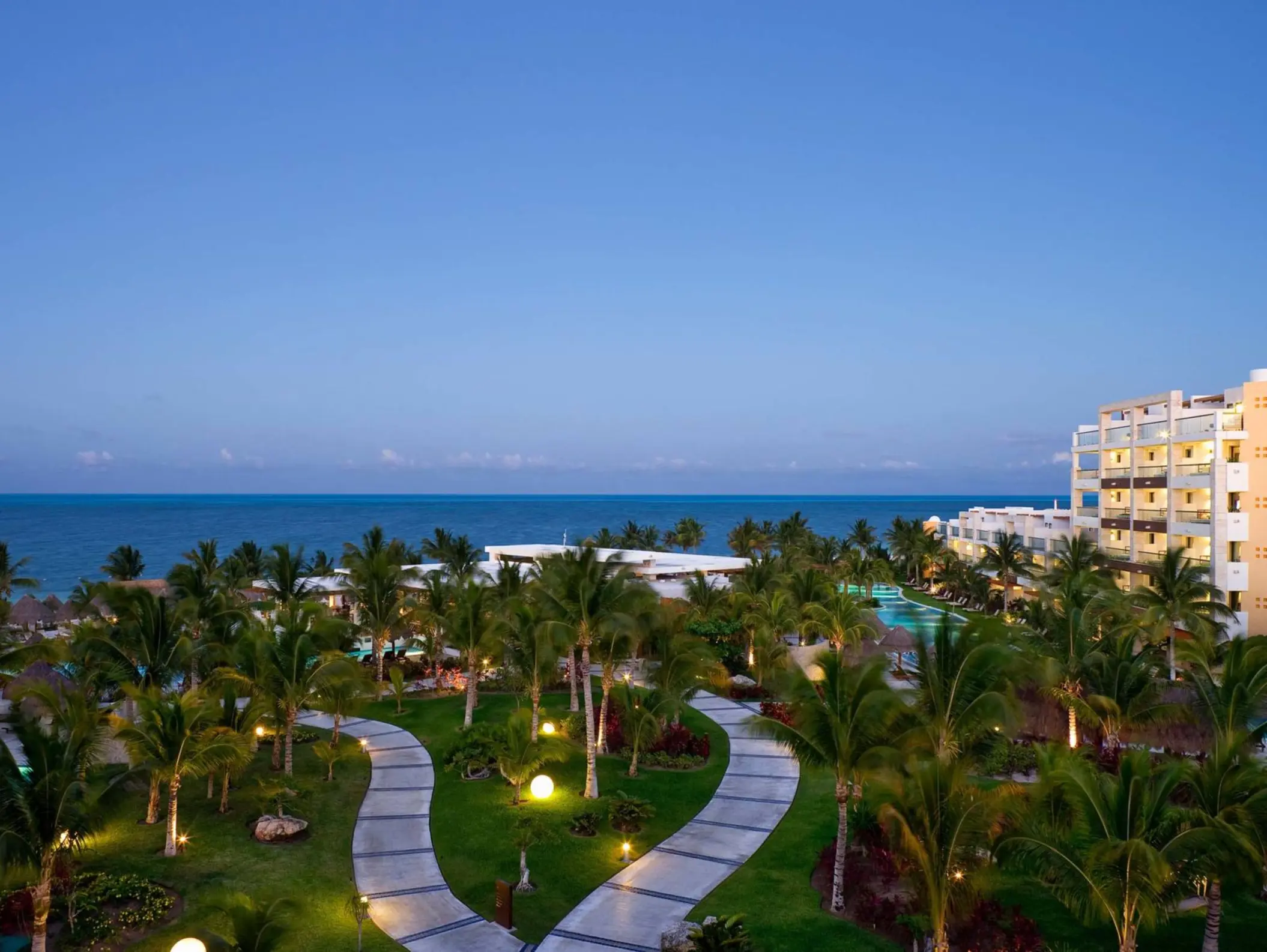Twilight view over manicured resort gardens, ocean horizon, and suite balconies in Cancun.