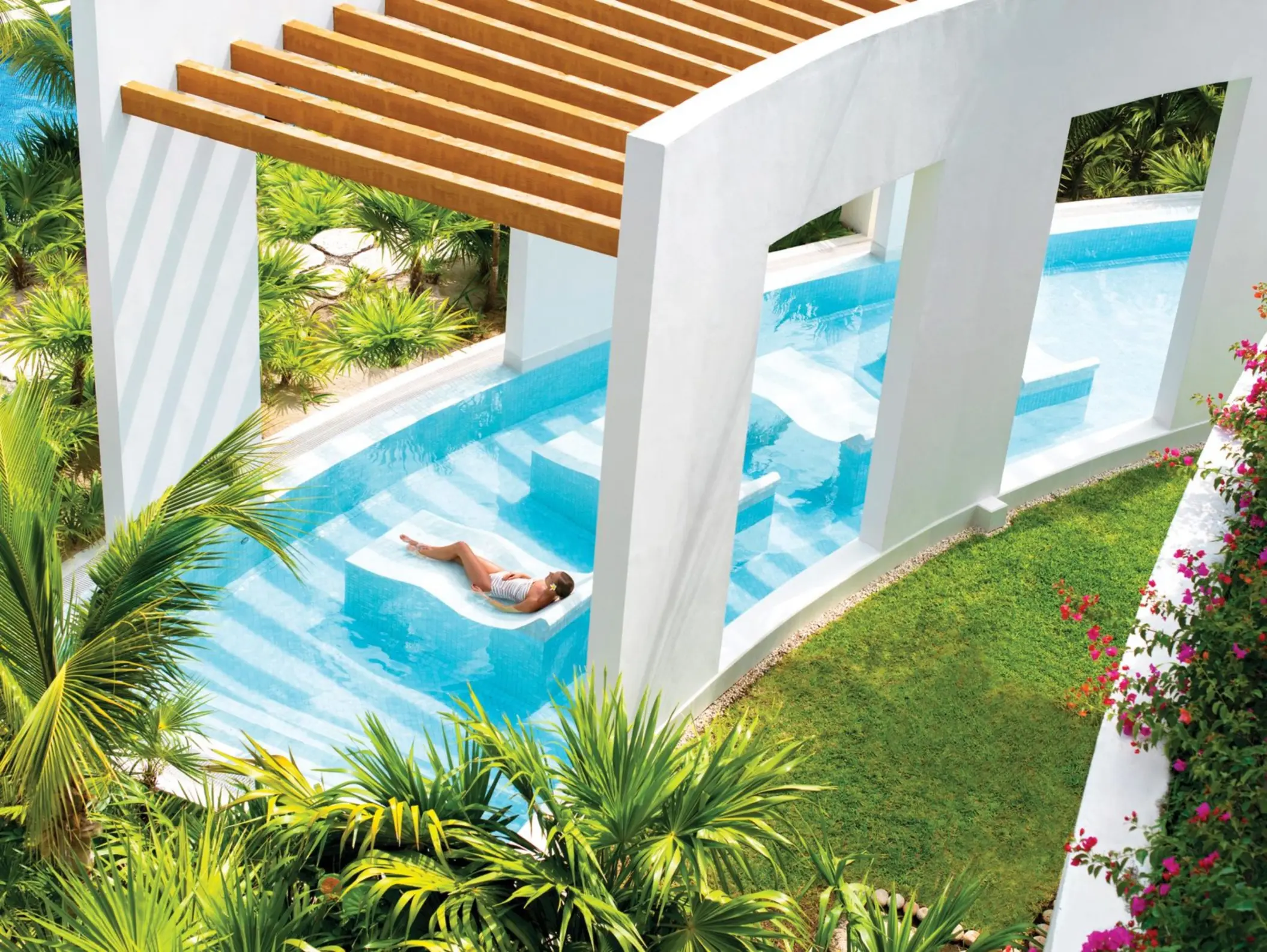 Woman lounging in a serene hydrotherapy circuit with lush landscaping at a Cancun luxury spa resort.