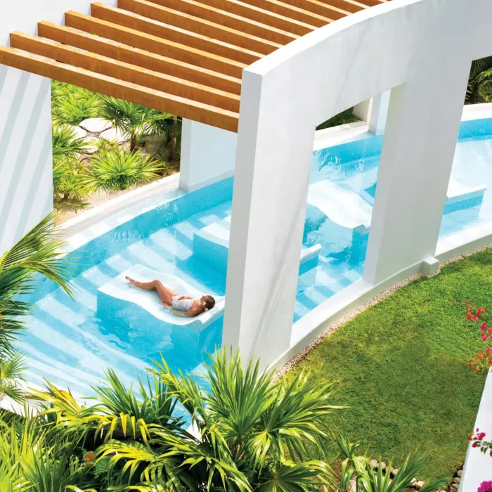 Woman lounging in a serene hydrotherapy circuit with lush landscaping at a Cancun luxury spa resort.